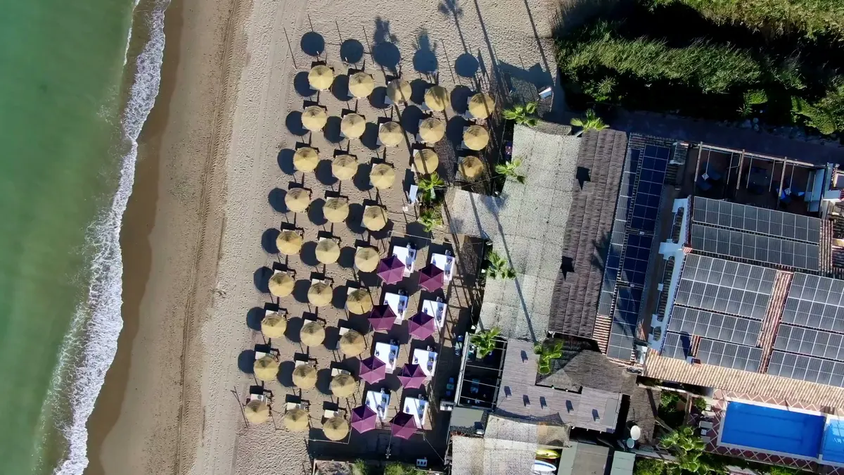 Overhead view of thatched sun umbrellas and cabanas on the sand beside the restaurant