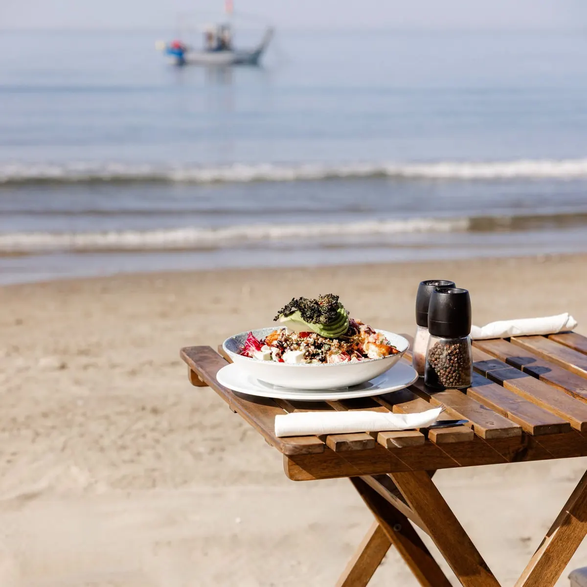 A beach table set with lunch at the water’s edge