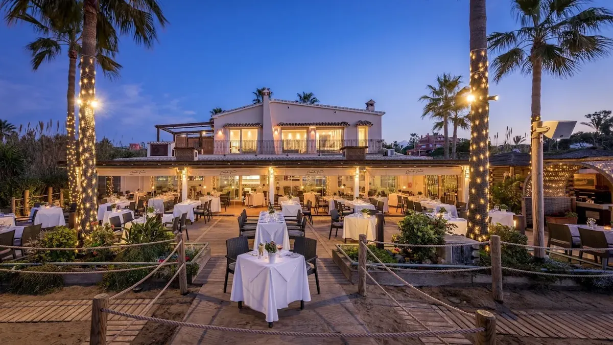 The restaurant terrace lit at dusk beneath palm trees