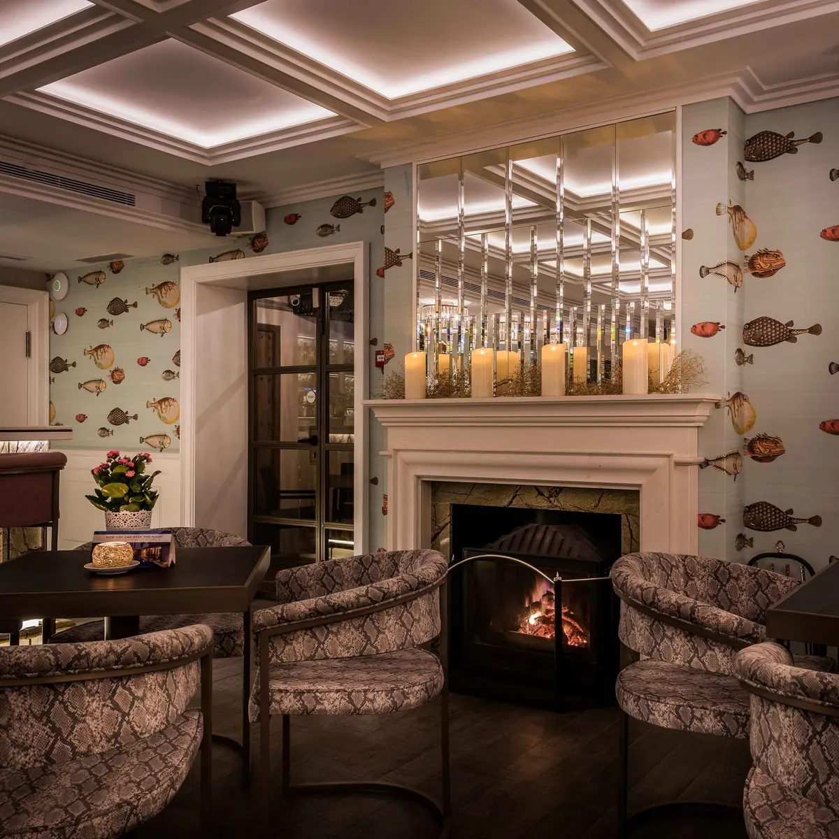 The interior lounge with a lit fireplace and fish-print wallpaper