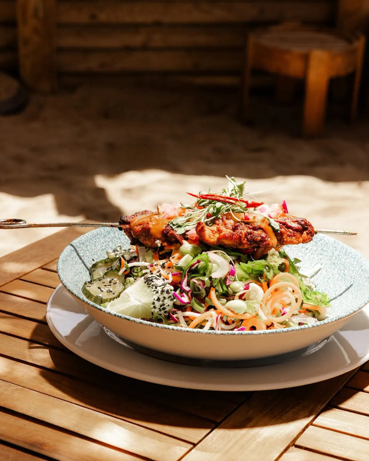 A chicken skewer over a noodle salad in sunshine