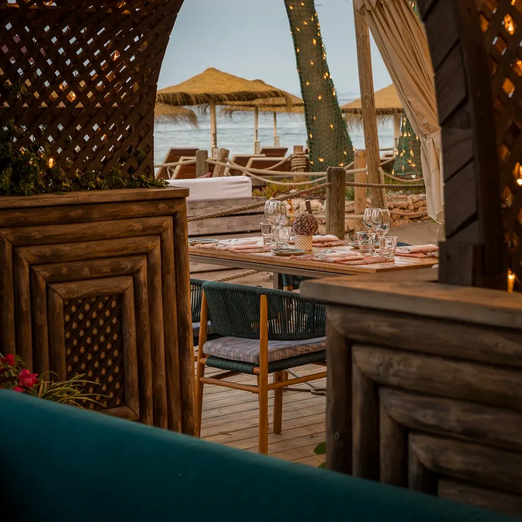 Dining terrace under carved timber screens looking out to the beach umbrellas and sea