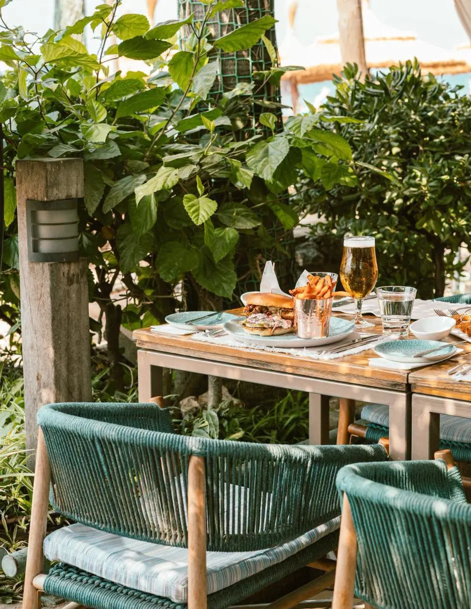 A terrace table set among tropical planting with lunch and a cold beer