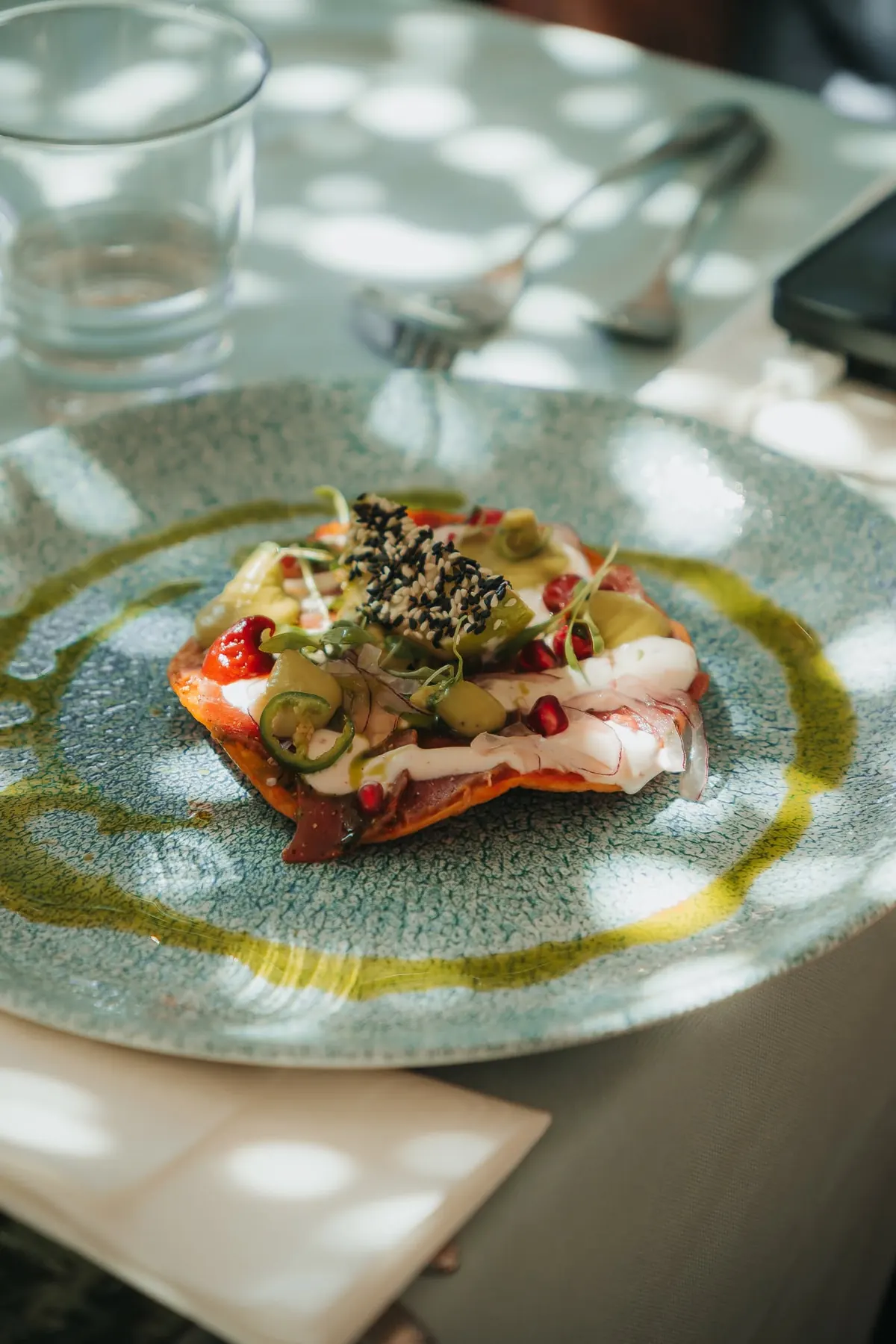 A raw fish dish dressed with herb oil in dappled sunlight